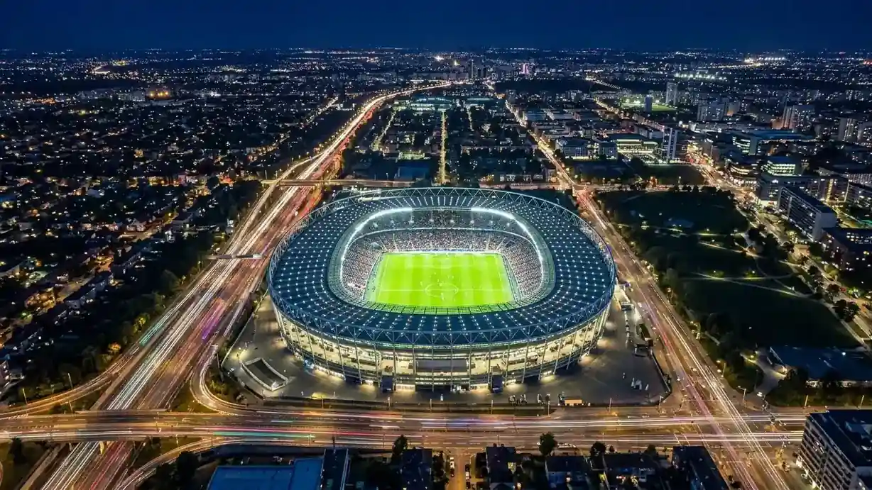 Vue aérienne nocturne d'un grand stade de football illuminé, entouré des lumières d'une ville