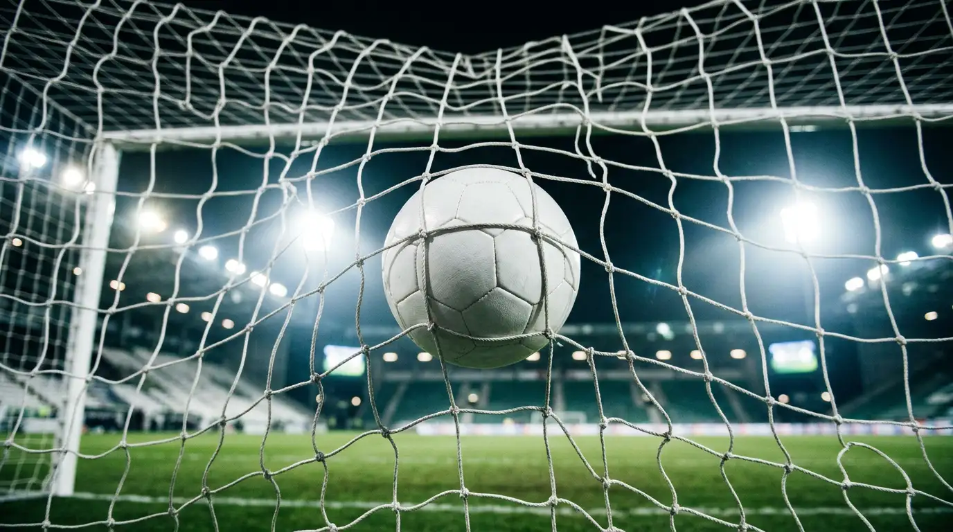 Ballon de football au fond des filets, vu de l'intérieur du but, sous les projecteurs d'un stade