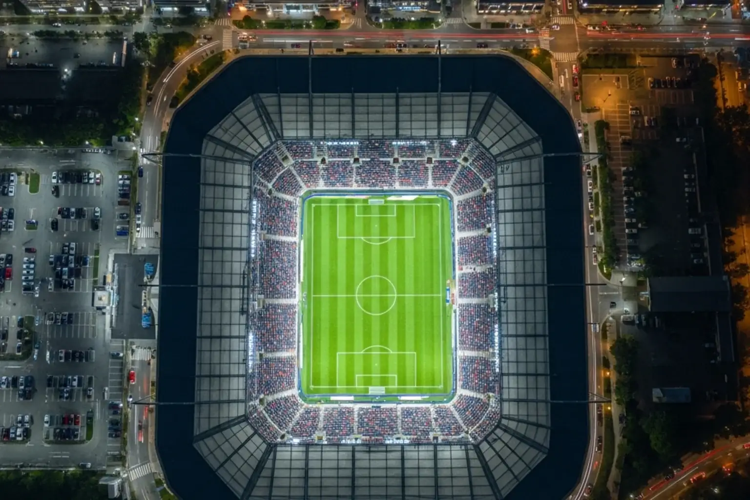 Vue aerienne d'un stade de football moderne illumine en soiree avec le terrain vert et les tribunes remplies de spectateurs